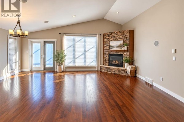 Living room with vaulted ceiling, dark wood floors, and a stone-clad gas fireplace. - 497 Edinburgh Road W, Lethbridge