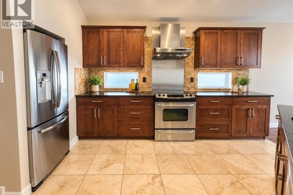 Kitchen detail showing stainless steel refrigerator, gas range, and dark wood cabinets. - 497 Edinburgh Road W, Lethbridge