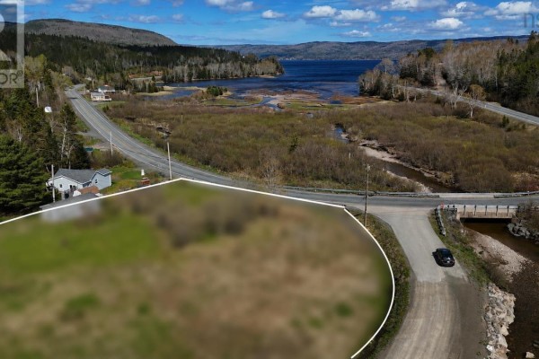 Aerial view of a cleared lot with a road and bridge in the foreground and a large body of water beyond. - 49740 Cabot Trail, Goose Cove