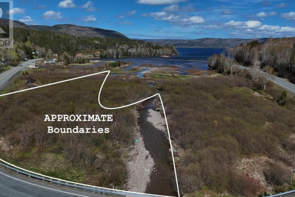 Aerial view shows property boundaries outlined in white, with a creek and marshland leading to a wide bay. - 49740 Cabot Trail, Goose Cove