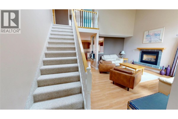 Carpeted staircase leading upstairs next to a living room with leather furniture and fireplace. - 4978 Timberside Place, Invermere