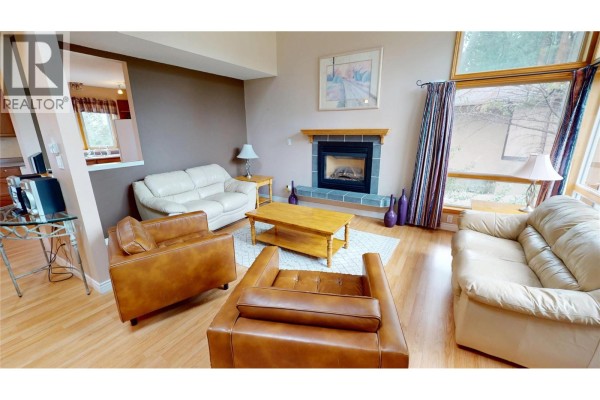 Living room with two white sofas, two brown leather chairs, a wooden coffee table, and a fireplace. - 4978 Timberside Place, Invermere