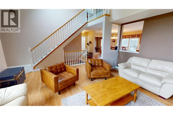 Living room with a large staircase, white sofas, brown leather armchairs, and a view into a dining area. - 4978 Timberside Place, Invermere