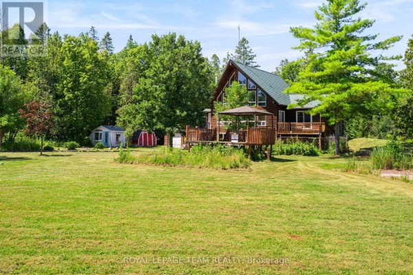 Front view of a log home with a steep green roof, many large windows, and a balcony. - 4984 Dunrobin Road, Ottawa
