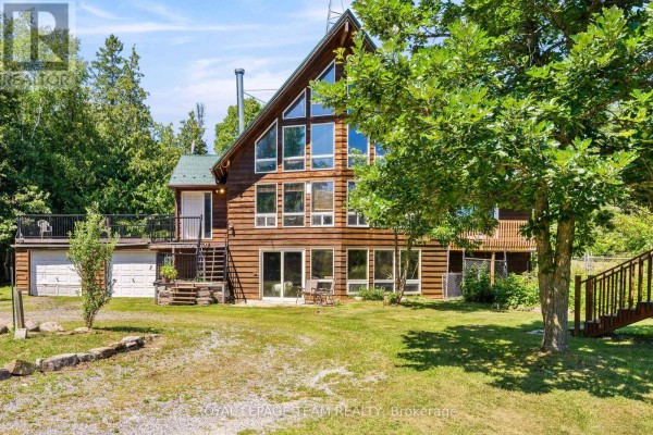 Back view of a log home with a large wooden deck, surrounding trees, and a grassy lawn. - 4984 Dunrobin Road, Ottawa