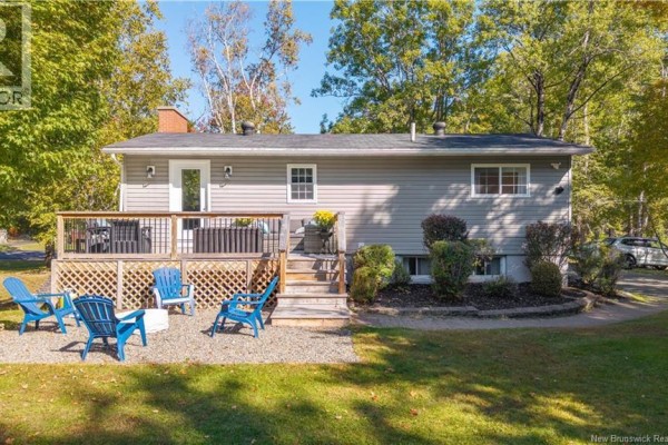 The rear of the grey bungalow with a wooden deck and blue chairs on the gravel patio. - 499 Ledge Road, Dufferin