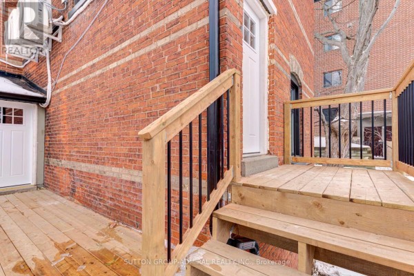 Wooden deck and stairs with black railings leading to a white door on a brick house. - 4u - 167 Collier Street, Barrie