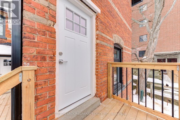 White paneled door with a silver handle on a brick wall, with a wooden deck in the foreground. - 4u - 167 Collier Street, Barrie