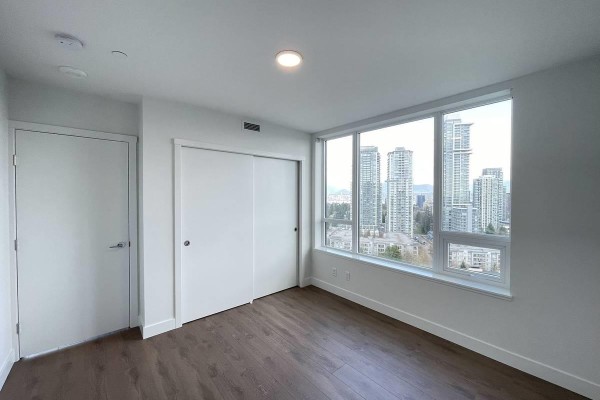 Bedroom with white sliding closet doors, large windows with city views, and wood-look flooring. - 4xx 13359 Old Yale Rd, Surrey