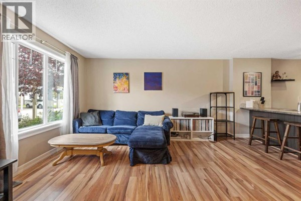 Living room with a large blue sectional sofa, coffee table, wood laminate flooring, and a large window. - 5, 133 Copperpond Heights Se, Calgary
