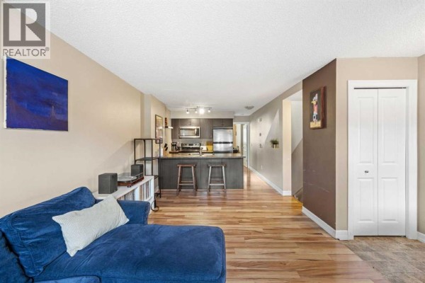 Open concept living area with a blue sectional, view of the kitchen, wood laminate floors, and a staircase. - 5, 133 Copperpond Heights Se, Calgary