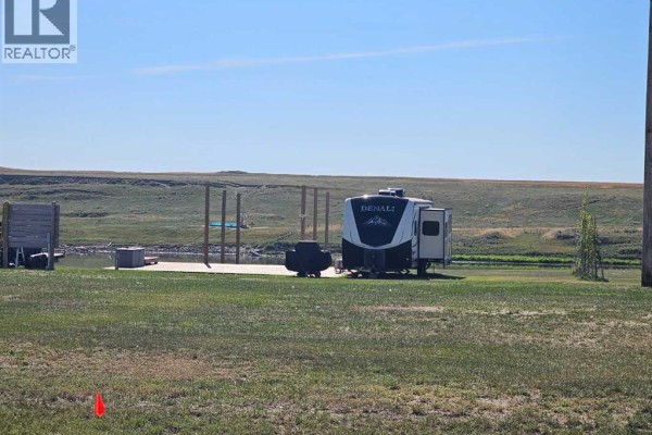 Close-up of RV on a grassy lot with wooden posts and distant hills. - 5, 172039 Hwy 539, Bow City