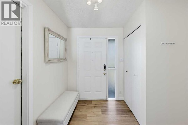 Interior entryway with a white door, bench, mirror, and wood-look flooring. - 5, 64 Woodacres Crescent Sw, Calgary