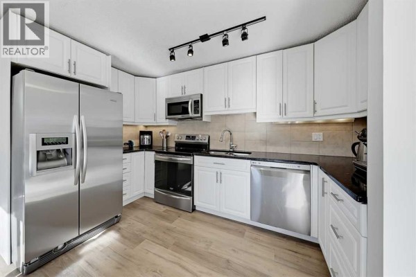 Modern kitchen with white cabinets, stainless steel appliances, and black countertops. - 5, 64 Woodacres Crescent Sw, Calgary