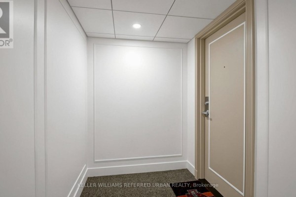 Hallway entrance to a unit with a neutral-colored door, white walls, and a small rug. - 5 - 1 Watergarden Way, Toronto