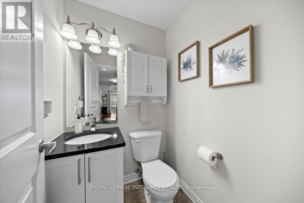 A powder room with a white vanity, black countertop, toilet, and two framed botanical prints. - 5 - 100 Prestige Circle, Ottawa