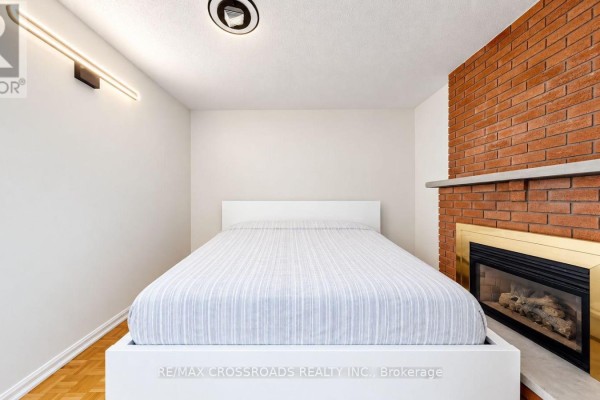 Bedroom with a white platform bed and a brick fireplace with gold trim. - 5 - 106 Stilecroft Drive, Toronto