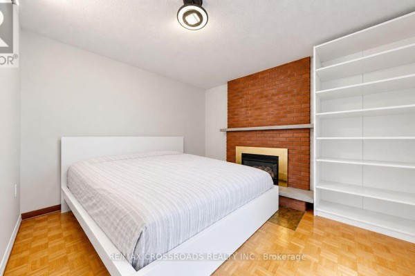 Bedroom with a white platform bed, brick fireplace, and white built-in bookshelf. - 5 - 106 Stilecroft Drive, Toronto