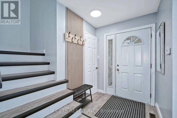 Entrance foyer with light blue walls, double white doors, wood slat accent wall, and stairs. - 5 - 1460 Limberlost Road, London North