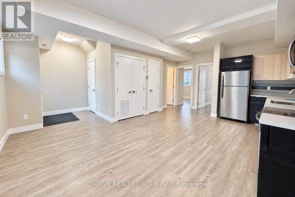 Interior view of an open-concept living area with light wood floors, doors, a stainless steel refrigerator, and a kitchen counter. - 5 - 147 Pond Mills Road S, London South