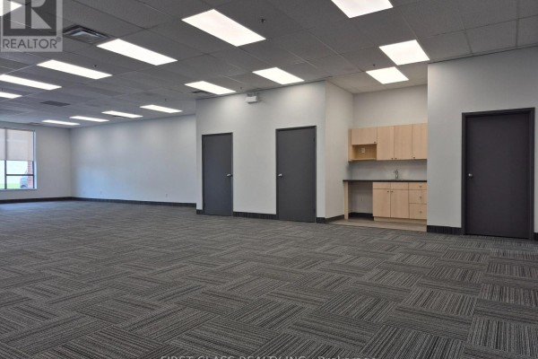Office interior with grey patterned carpet, kitchenette with light wood cabinets, and dark grey doors. - 5 - 20 Steelcase Road W, Markham