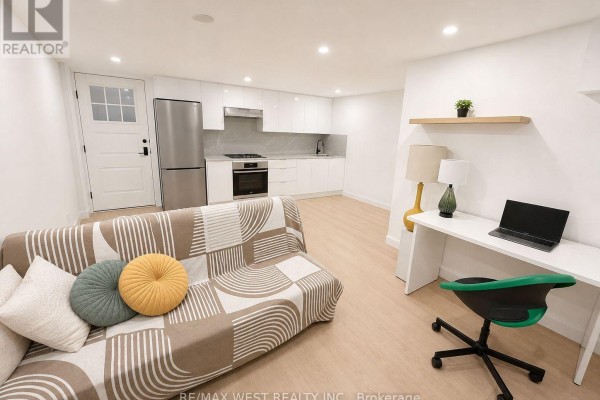 Basement living area with sofa, desk, and white kitchen cabinets with stainless steel appliances. - 5 - 202 Perth Avenue, Toronto
