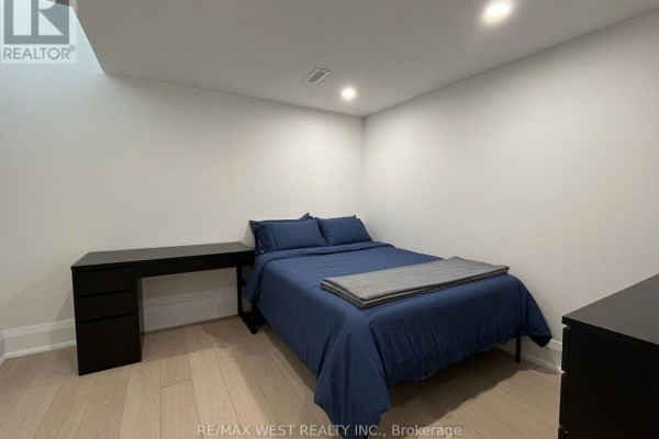 Bedroom with a queen-size bed, blue bedding, and a black desk against a white wall. - 5 - 202 Perth Avenue, Toronto
