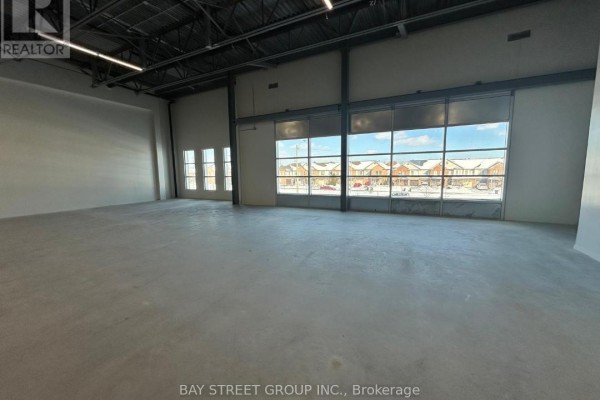 Expansive commercial interior with concrete floors, steel beams, and large windows with an exterior view of houses. - 5 - 2560 Morningside Avenue, Toronto