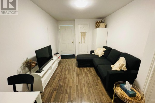 Living room with a black sectional sofa, white media console, and television, with wood-look flooring. - 5 - 296 Runnymede Road, Toronto