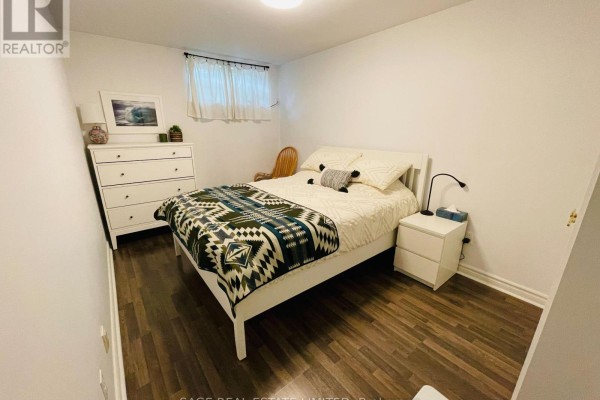 Bedroom with a queen bed, white dresser, and a chair, featuring dark wood-look flooring. - 5 - 296 Runnymede Road, Toronto