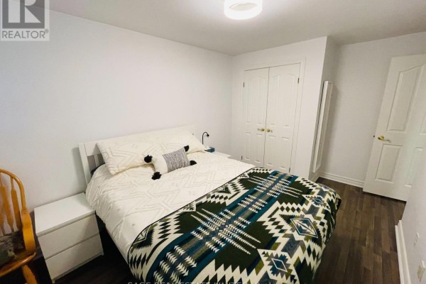 Bedroom with a queen bed, white nightstands, and white double doors, featuring dark wood-look flooring. - 5 - 296 Runnymede Road, Toronto