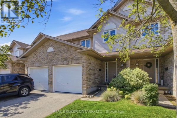 Entrance to a townhouse featuring a small porch, beige brickwork, and dual garage doors. - 5 - 31 Schroder Crescent, Guelph