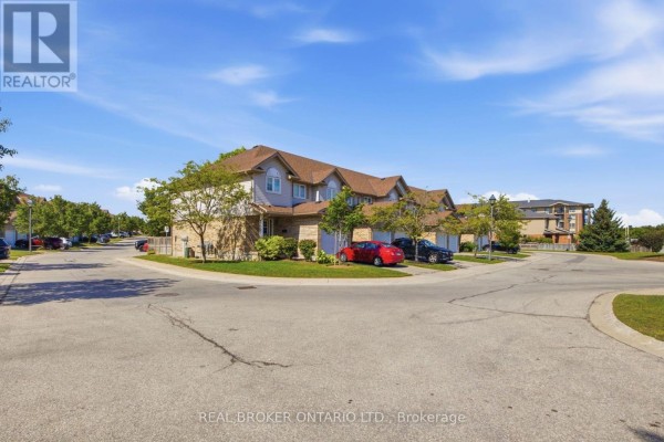 Street view of a townhouse complex on a corner lot with parked cars and blue sky. - 5 - 31 Schroder Crescent, Guelph