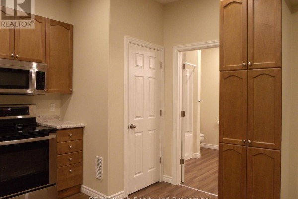 Kitchenette with wooden cabinets, stainless steel appliances, and an open doorway revealing a bathroom. - 5 - 350 Dundas Street, Woodstock