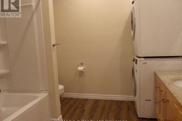 Bathroom with white bathtub, toilet, stacked washer and dryer, and wooden vanity with granite countertop. - 5 - 350 Dundas Street, Woodstock