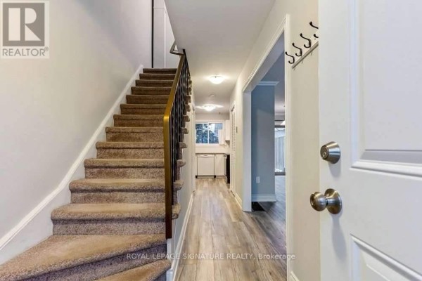 Entryway with a white door, staircase, and a hallway leading to the kitchen. - 5 - 46 Mountainview Road S, Halton Hills