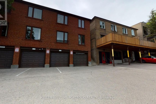 Rear view of a brick apartment building with multiple garages and an elevated wooden deck. - 5 - 546 Eglinton Avenue E, Toronto