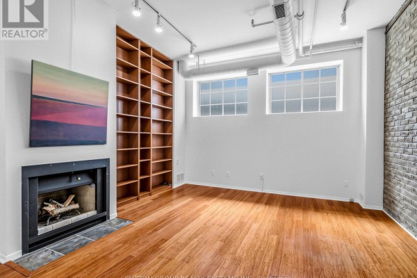 Living room featuring a fireplace, built-in bookshelf, hardwood floors, white walls, and exposed ductwork. - 5 - 6 Bartlett Avenue W, Toronto
