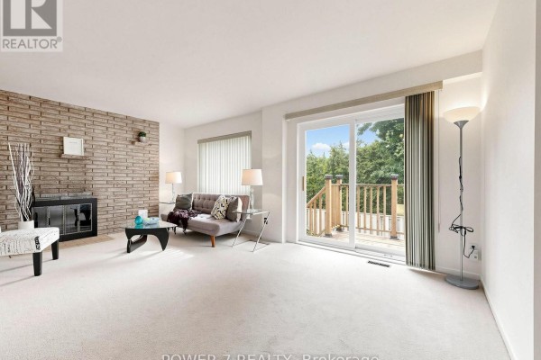 Living room with a brick fireplace, sofa, coffee table, and sliding glass doors to a deck. - 5 - 77 Rameau Drive, Toronto