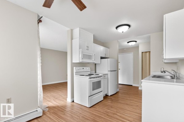 Open concept kitchen with white cabinets, white appliances including a stove and refrigerator, and wood laminate flooring. - #5 11265 31 Av Nw, Edmonton