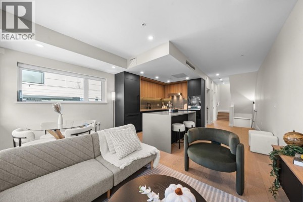Living room with grey couch, green armchair, and open-concept kitchen. - 5 128 W Woodstock Avenue, Vancouver