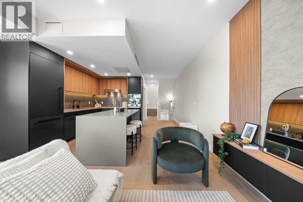 View of the kitchen island, dining area, and living room with wood accent wall. - 5 128 W Woodstock Avenue, Vancouver