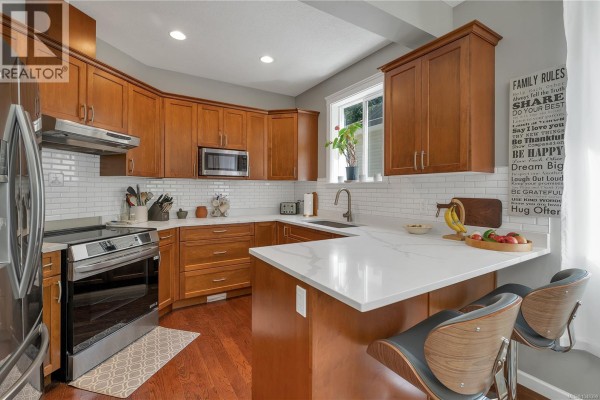 Modern kitchen with wood cabinets, white countertops, stainless steel appliances, and island seating. - 5 1424 Alder St S, Campbell River