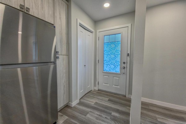 View of the front door with a white frame and frosted glass. A stainless steel refrigerator is to the left. - 5 235 Glen Avenue, Brandon