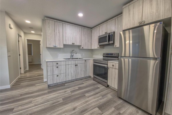 L-shaped kitchen with light wood cabinets, white countertops, stainless steel appliances and a double sink. - 5 235 Glen Avenue, Brandon