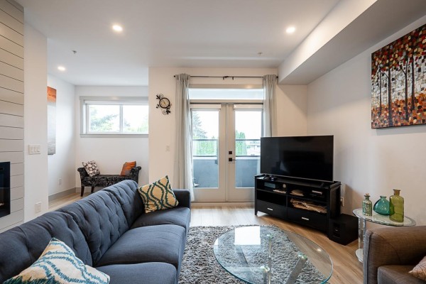 Living room with a large blue sofa, glass coffee table, media console with television, and glass doors. - 5 46545 Brooks Avenue, Chilliwack Proper South, Chilliwack