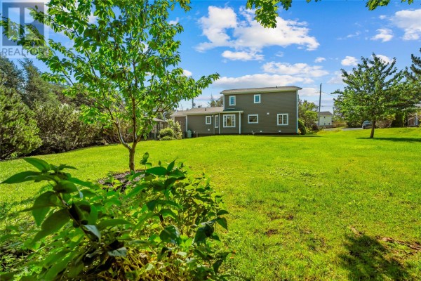 Rear view of the home with a large green lawn and mature trees under a blue sky. - 5-7 Spelling Hill Road, Burin Bay Arm