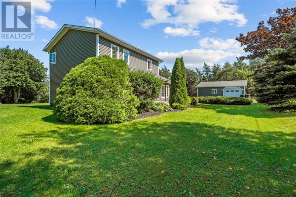 Side of the house with grey siding, mature trees, shrubs, and a detached garage. - 5-7 Spelling Hill Road, Burin Bay Arm