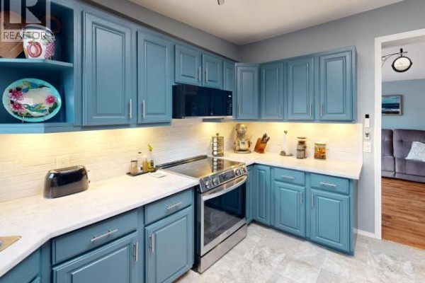 Kitchen with teal cabinets, white subway tile backsplash, and stainless steel appliances. - 5-8442 Springbrook Road, Powell River