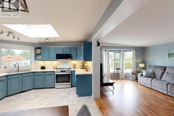 Open concept living space showing the kitchen and living room with blue walls and wood floors. - 5-8442 Springbrook Road, Powell River